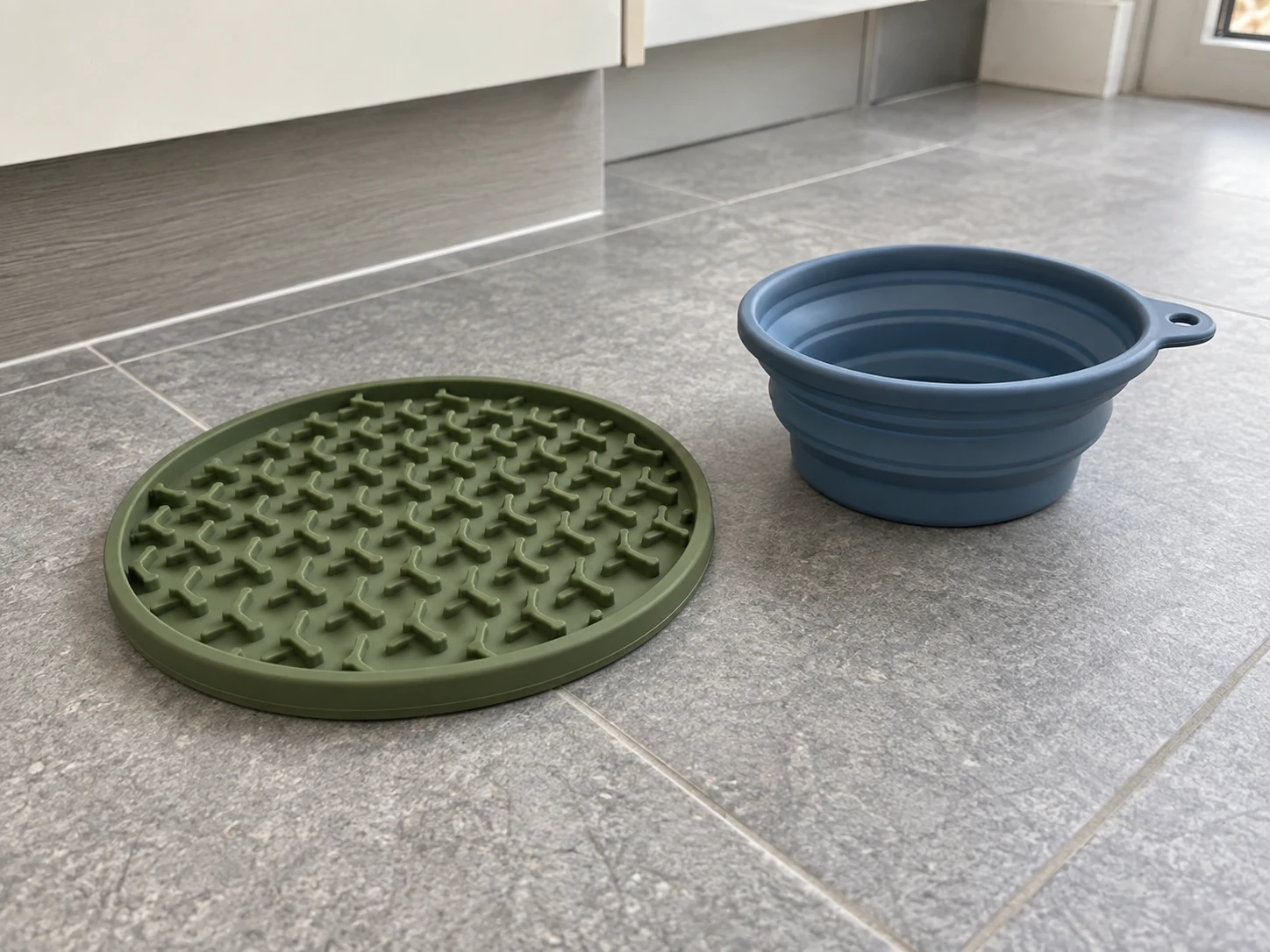 Green silicone lick mat and blue collapsible bowl on a tiled floor